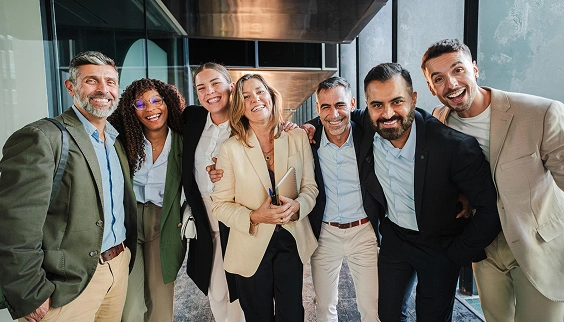 Diverse group of business professionals smiling together in a modern office corridor.